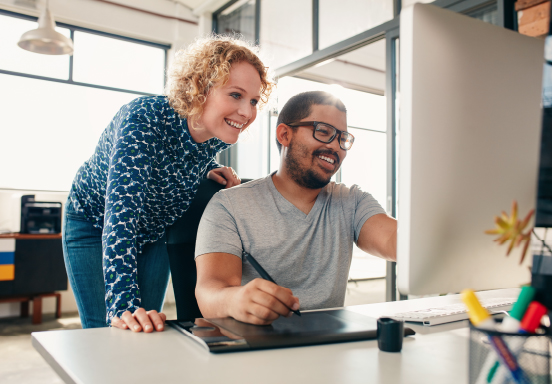 Colleagues smiling while working together at a computer in a modern office
